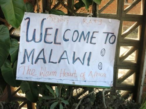 Ein selbst gemaltes Plakat mit der Aufschrift "Welcome to Malawi" an einem begrünten Zaun.